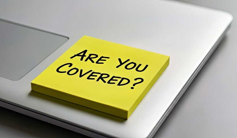 A couple reviews insurance documents beside a laptop and home inventory checklist at a kitchen table.
